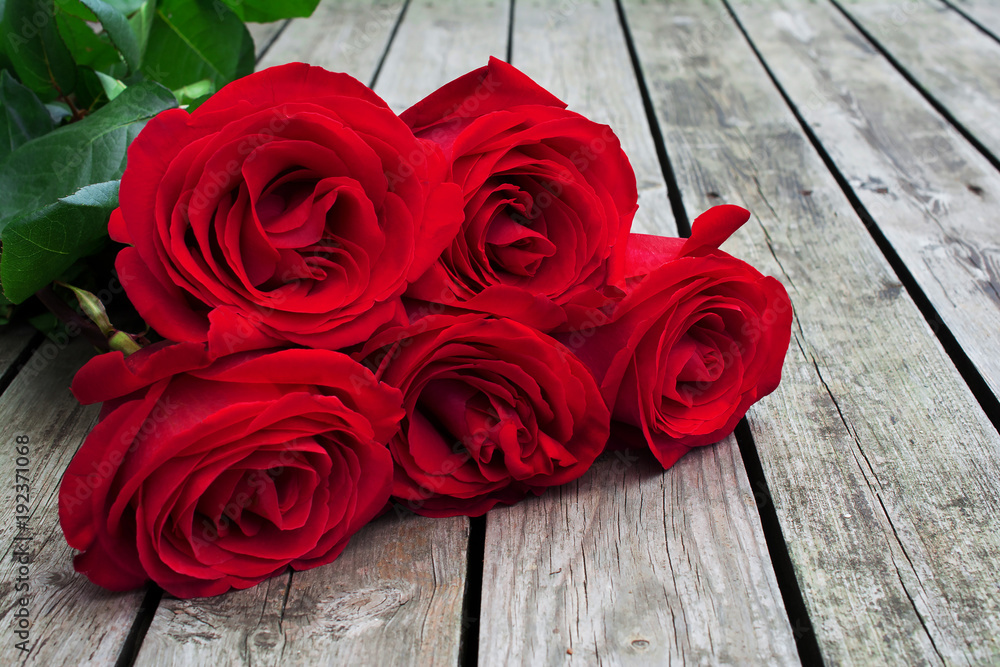 Red or scarlet bunch of roses with green leaves on background of rough wooden gray planks. Red or scarlet bunch of roses with green leaves on background of rough wooden gray planks.