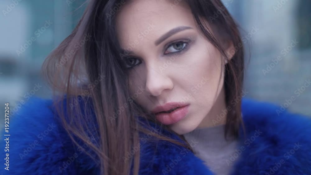 Beautiful girl in coat outdoors, in cold weather. In the background glass skyscraper. Slow mo. Cute female model enjoy. Closeup. Pleasant girl wrapped in fur coat from cold, flirting, look intently. Beautiful girl in coat outdoors, in cold weather. In the background glass skyscraper. Slow mo. Cute female model enjoy. Closeup. Pleasant girl wrapped in fur coat from cold, flirting, look intently.