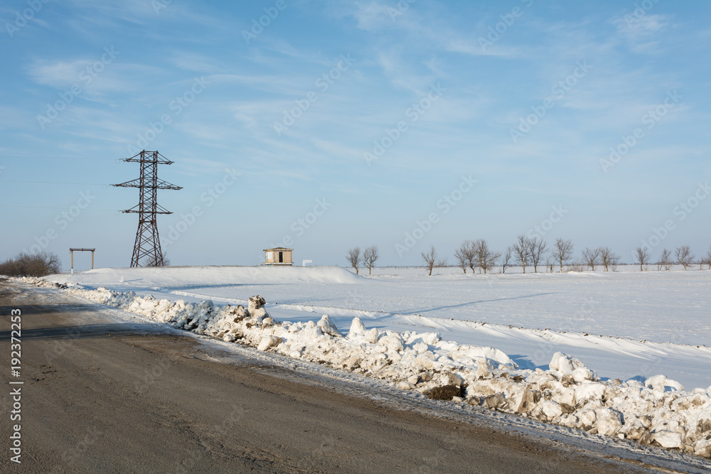 Electrical power line pillar on snow in front of blue sky and clouds