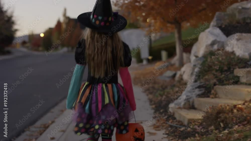 Rear view tracking shot of girl wearing witch costume walking in neighborhood / Cedar Hills, Utah, United States Rear view tracking shot of girl wearing witch costume walking in neighborhood / Cedar Hills, Utah, United States