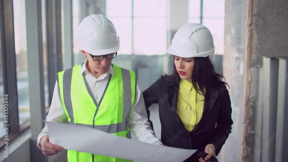 Man and Woman Engineers Have Conversation and Looking at Large Blueprint. 4 k green vests Man and Woman Engineers Have Conversation and Looking at Large Blueprint. 4 k green vests