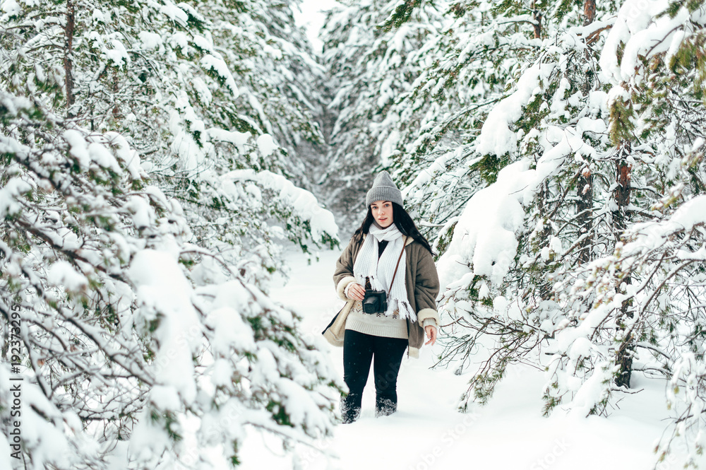 A beautiful girl walks through the snowy winter coniferous forest.