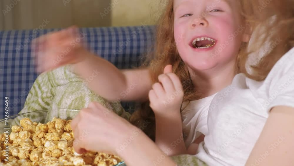 Happy loving family. Mother and her daughter child girl are eating popcorn on the bed in the room. front of the TV Happy loving family. Mother and her daughter child girl are eating popcorn on the bed in the room. front of the TV