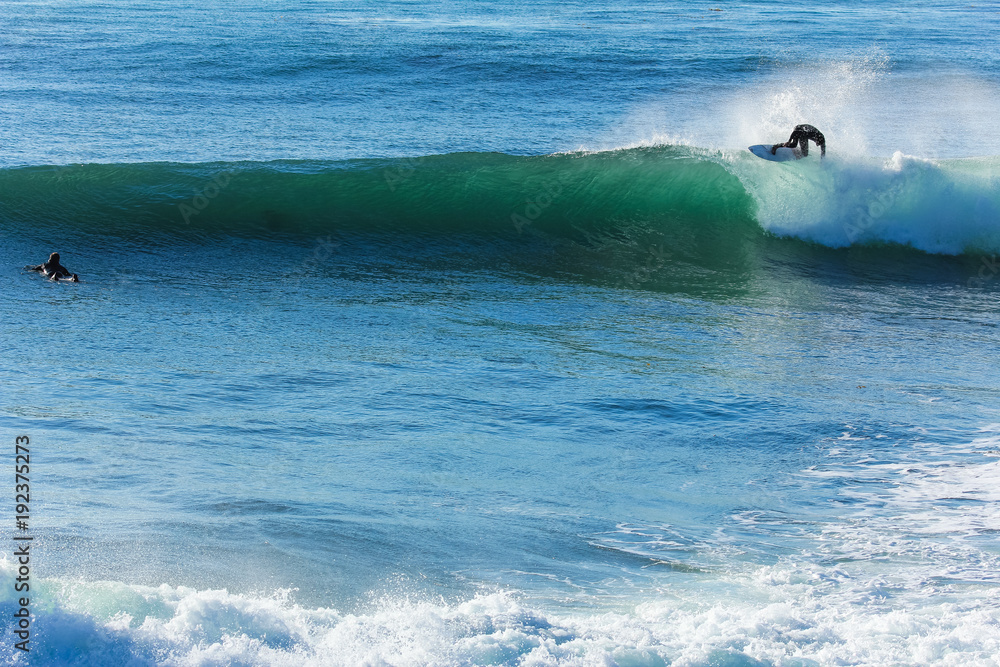 Surfer in California surfs large wave in beautiful blue water at beach Surfer in California surfs large wave in beautiful blue water at beach