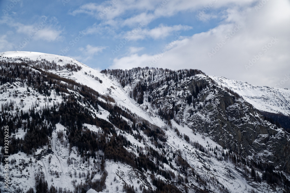 Mountains covered with snow, blue sky with clouds and winter forest near Mont Blanc Alpes, Italy Mountains covered with snow, blue sky with clouds and winter forest near Mont Blanc Alpes, Italy