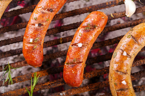 Close up of three grilling sausages on barbecue grill with some species. BBQ in the garden. Bavarian sausages photo