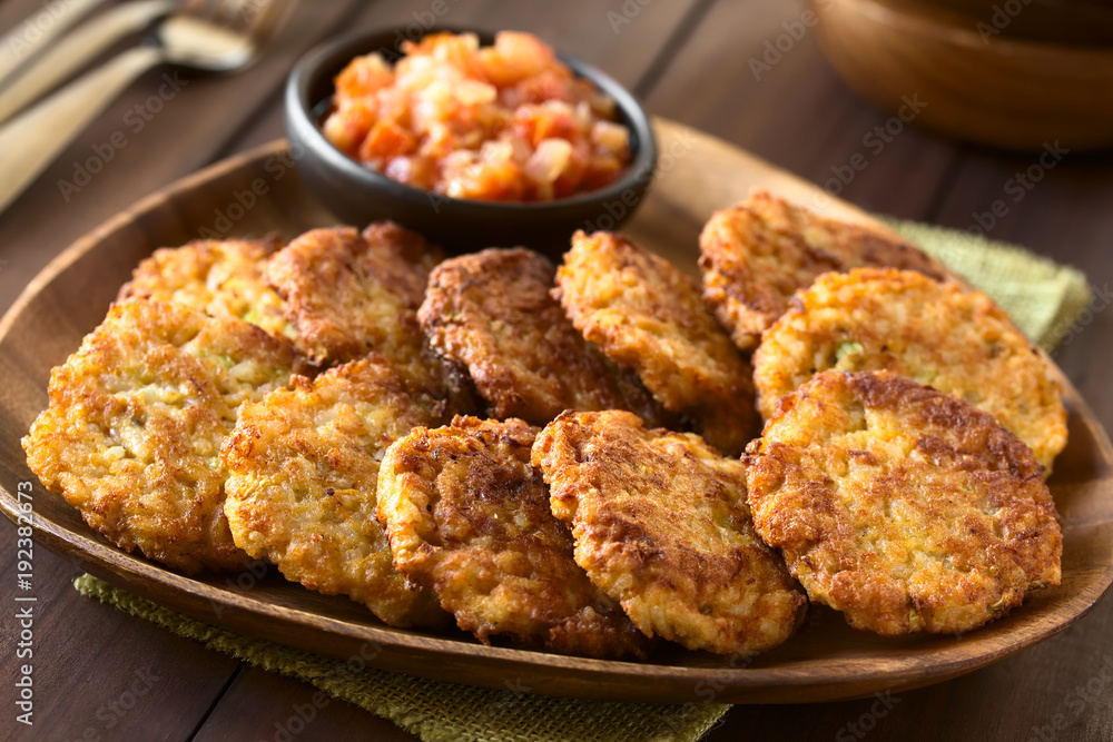 Rice patties or fritters made of cooked rice, carrot, onion, garlic and celery stalks, tomato sauce in the back, photographed with natural light (Selective Focus, Focus one third into the image)