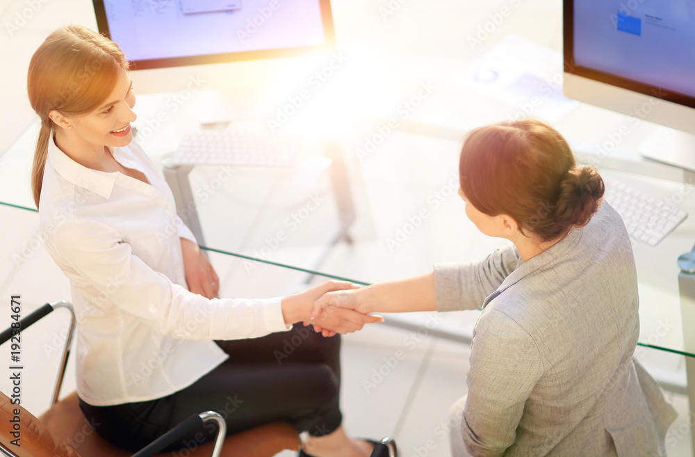 Obraz premium view from the top.business woman shakes hands with the officer sitting near the desktop