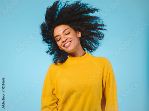 mixed race black woman portrait with big afro curly hair on blue background dancing and with hairstyle flying in air photo