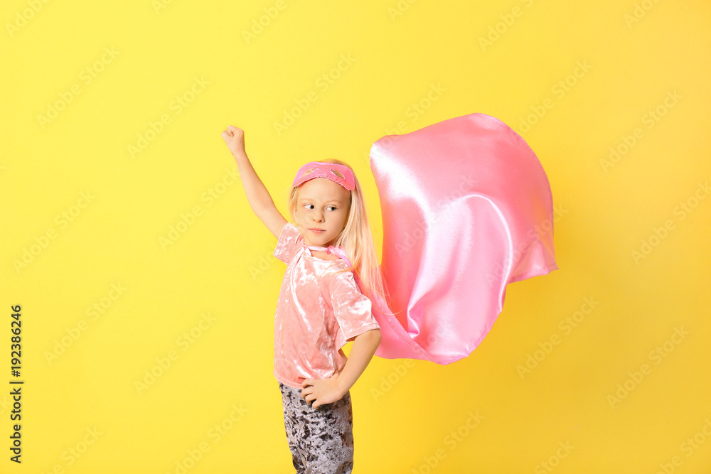 Cute girl in superhero costume on color background