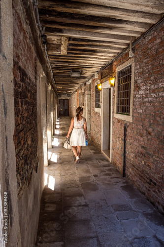 Frau in weißem Kleid geht durch schattige Gasse überdacht in Venedig © Michael Eichhammer