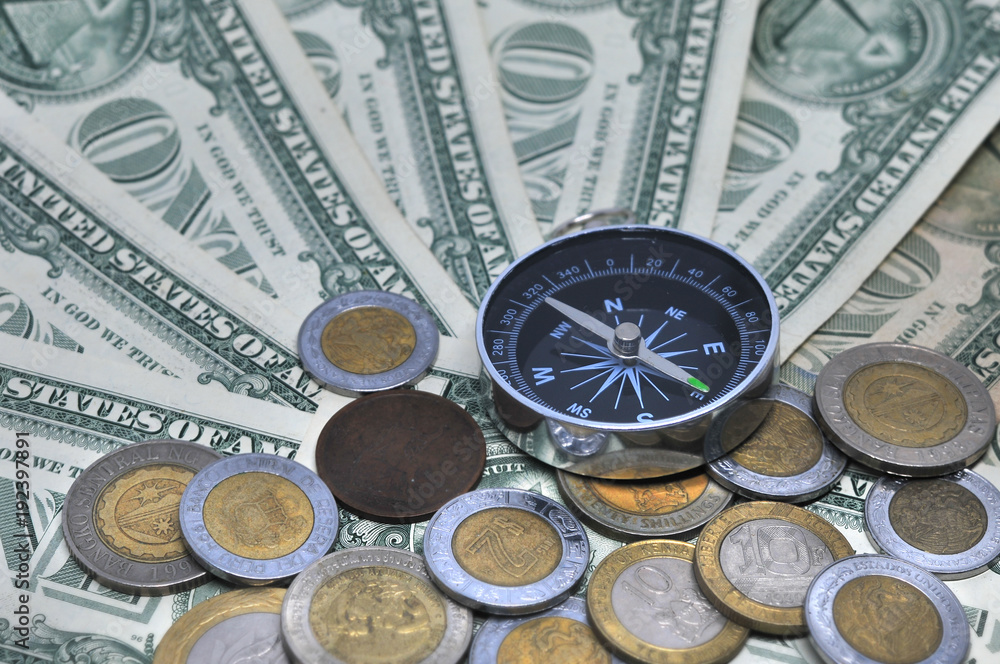 Compass and coins laying on a pile of on dollar bills
