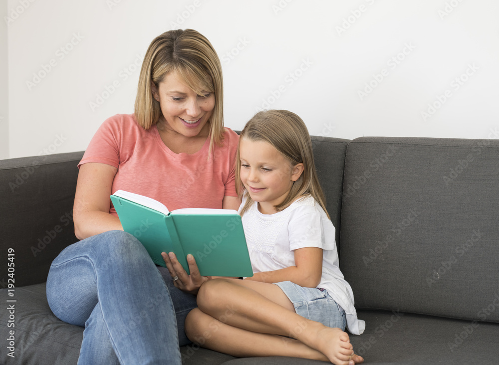 young beautiful and happy women sitting together with her adorable 7 years old adorable blond girl reading book enjoying telling story young beautiful and happy women sitting together with her adorable 7 years old adorable blond girl reading book enjoying telling story