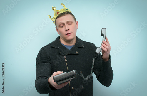 Foto Arrogant and smug hot line consultant or manager with golden crown above his head is talking on handset phone isolated on blue background