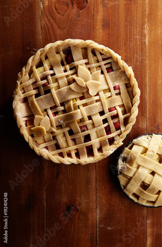 Pie crust design ideas - various ways of pie decoration with lattice and leaves. Apple, strawberry and raspberry pies uncooked on red wooden background.