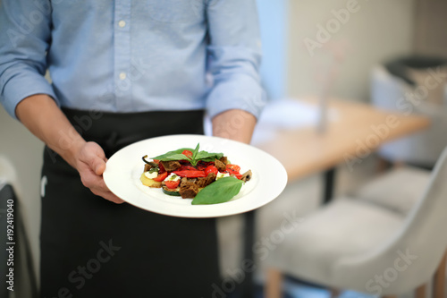 Waiter holding plate with vegetable salad indoors, closeup