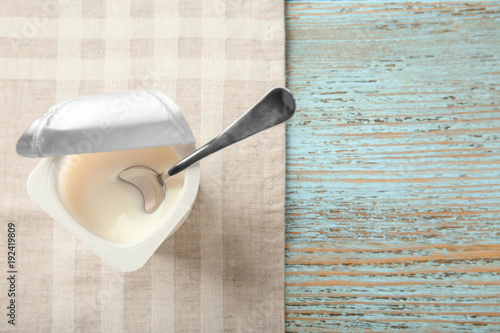 Plastic cup with yogurt on wooden background