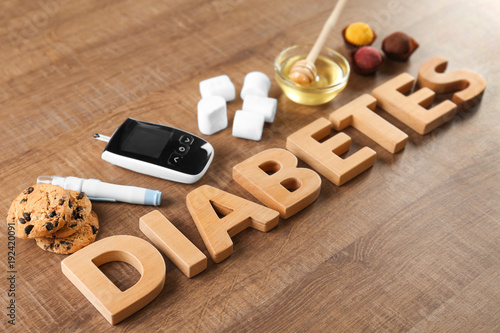 Composition with word "Diabetes", sweets and digital glucometer on wooden background