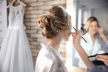 Makeup artist preparing bride before her wedding in room
