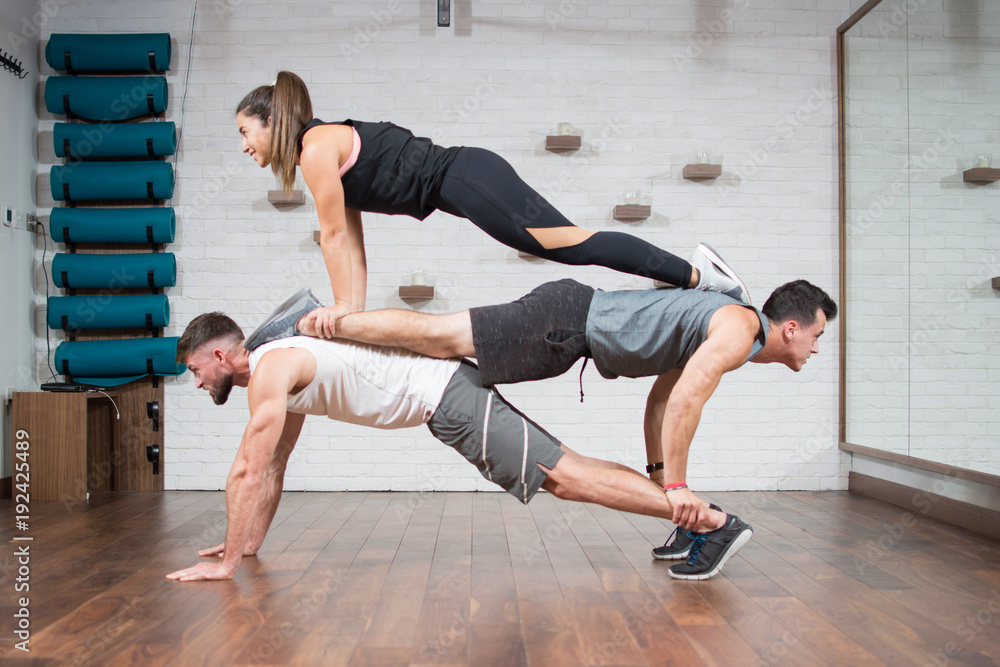 Group of three sporty people doing push-ups on each other in