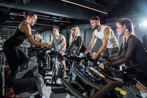 Female fitness instructor leading spinning class in gym.