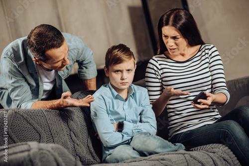 Clear explanation. Strict young parents telling their son about the drawbacks of binge-playing on the phone while the boy, scolding him, while the boy looking offended