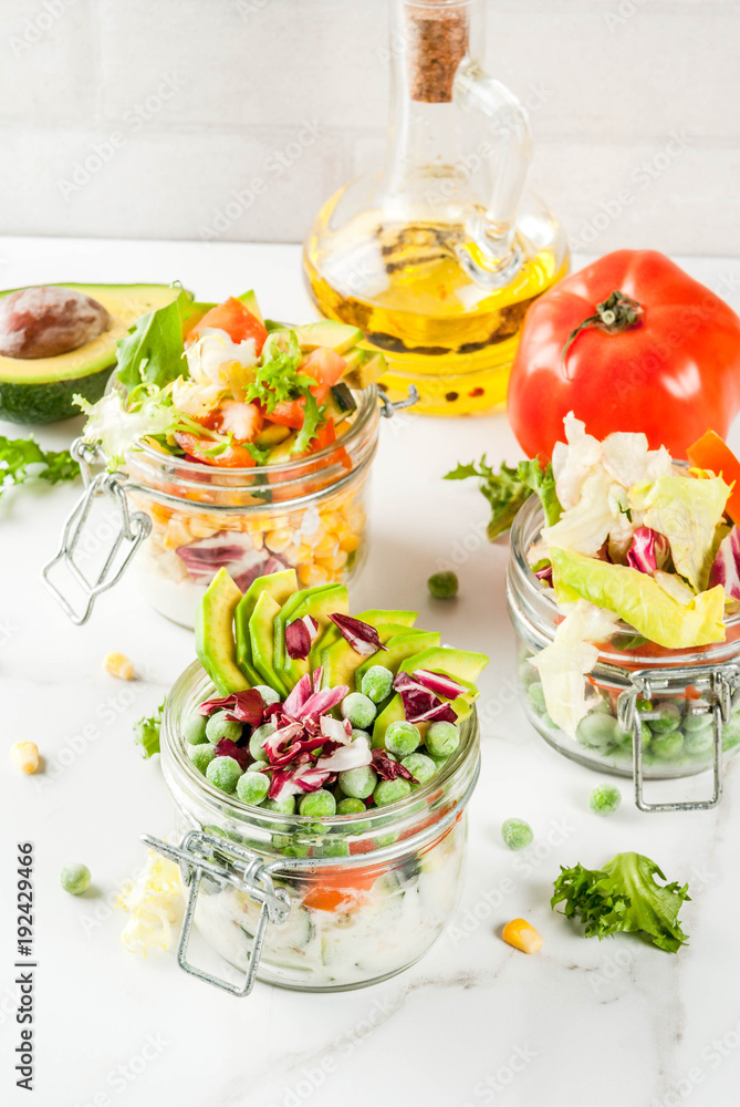 Fresh salads in jar with fresh vegetables and healthy dressings, on white marble table, copy space Fresh salads in jar with fresh vegetables and healthy dressings, on white marble table, copy space