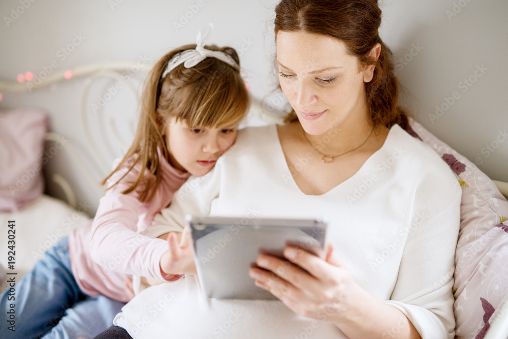 Mother and daughter looking at tablet, sitting on bed. Mother and daughter looking at tablet, sitting on bed.