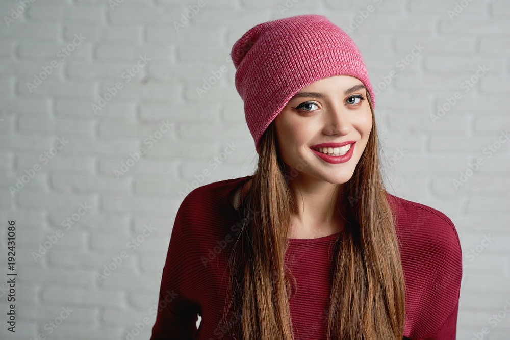 Studio portrait of a young smiling model, wearing pink cap and red sweatshot. Also she has light daily make-up with red lipstick. She looks very happy. Photo was taken on the grey background. Studio portrait of a young smiling model, wearing pink cap and red sweatshot. Also she has light daily make-up with red lipstick. She looks very happy. Photo was taken on the grey background.
