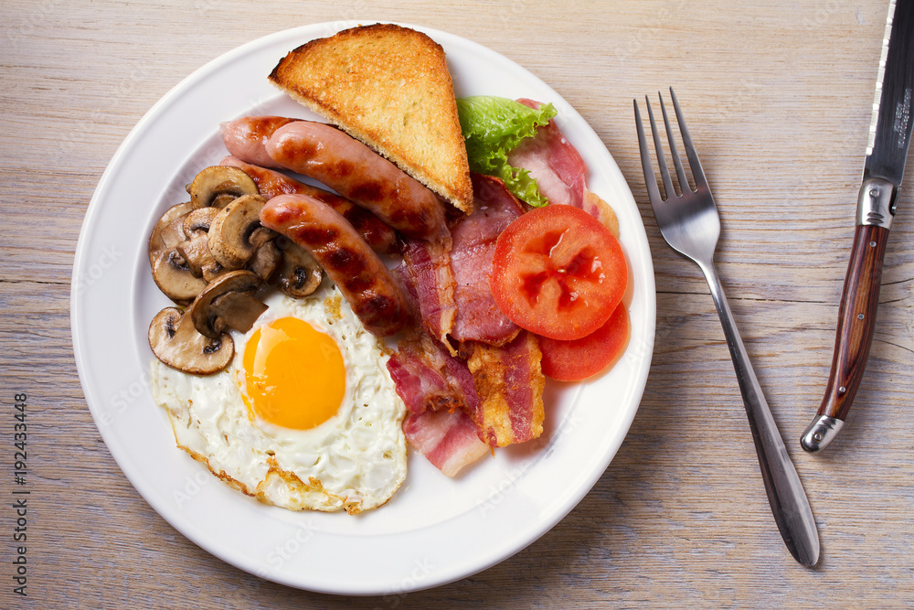 Full English or Irish breakfast: sausages, bacon, egg, mushrooms, tomatoes and toasts. Nutritious morning meal