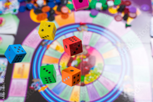 Several rolling color dice fall on a table with board game. Gaming moments in dynamics