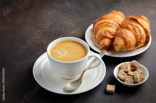 Cup of fresh coffee with croissants on dark background, selective focus