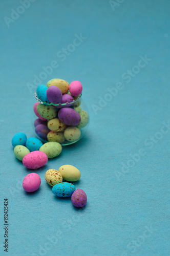 A small glass container filled with colorful speckled eggs on a blue background
