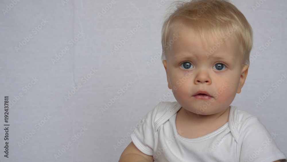 Naklejka premium Portrait of a beautiful little baby (boy), looks into the camera, blond, light-haired, blue eyes, white background. Concept: babies, fair skin, beautiful children.