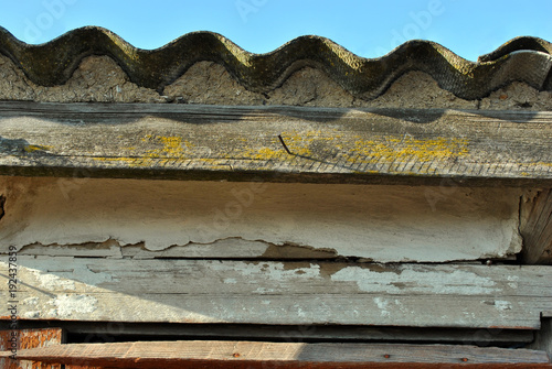 Slate barn roof with wavy line and shabby wooden plank with yellow moss on blue sky background