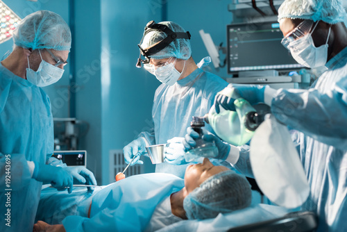 african american anesthetist holding oxygen mask above patient during surgery photo