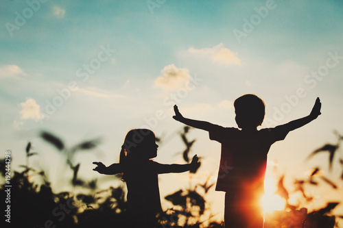 Obraz na plátně little boy and girl silhouettes play at sunset