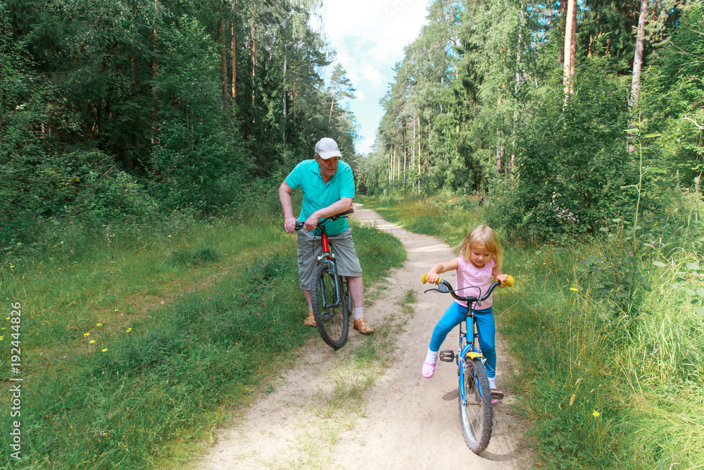 active senior with granddaughter riding bikes in nature active senior with granddaughter riding bikes in nature
