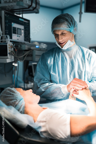 smiling doctor and patient holding hands in surgery room