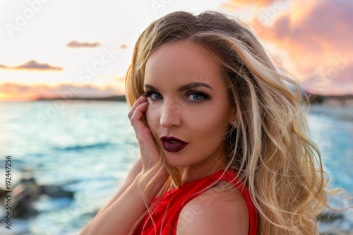 Portrait of beautiful elegant young blonde, posing in evening red dress on sea quay