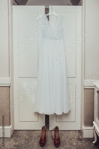 Suknia ślubna wisząca na białej szafie oraz buty.