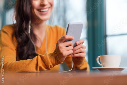 Advanced smartphone. Close up of tender young female hand hold phone while cup of tea standing on surface
