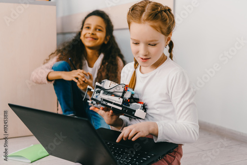 teen schoolgirls programming robot while sitting on floor
