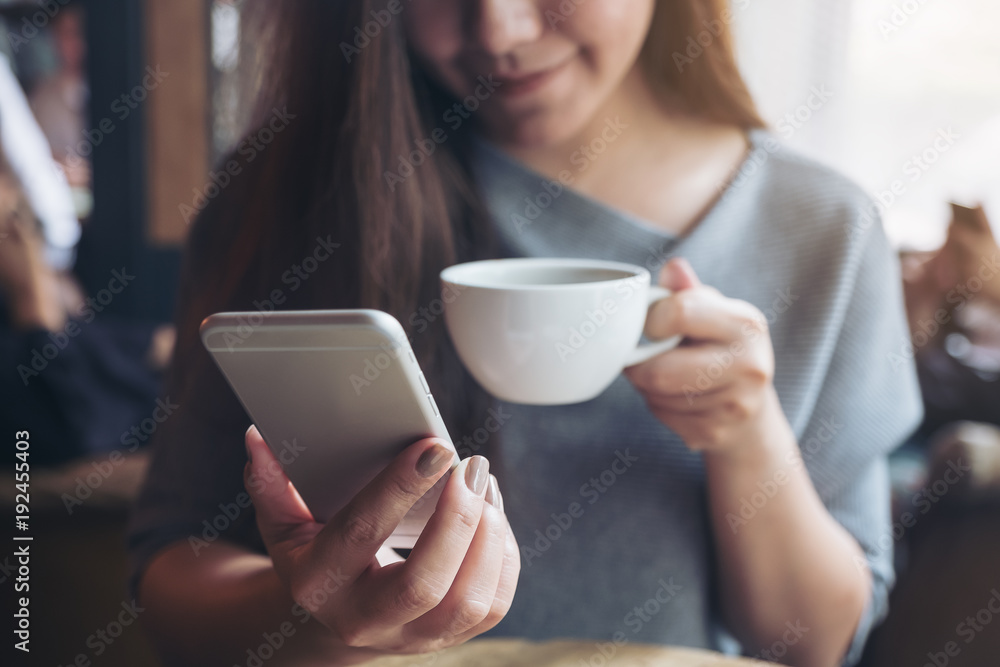Closeup image of a beautiful Asian woman holding and using smartphone while drinking coffee in cafe Closeup image of a beautiful Asian woman holding and using smartphone while drinking coffee in cafe