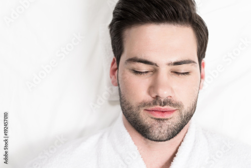 close-up view of handsome bearded man in bathrobe relaxing in spa salon