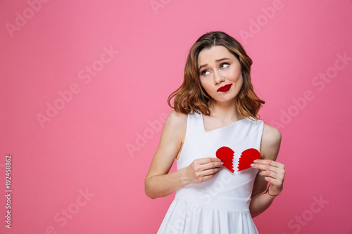 Confused woman holding broken heart. Looking aside.