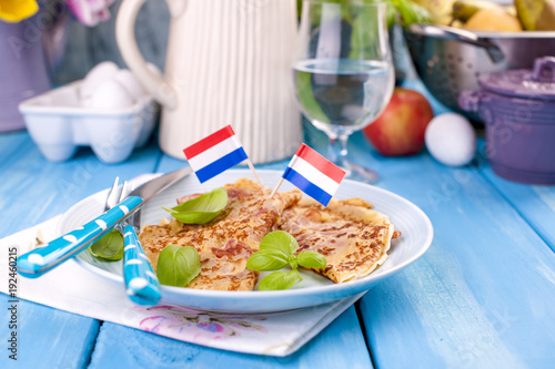 Homemade traditional pancakes with bacon or ham. Calorie meal. The Netherlands breakfast. Holland. Bright flowers of tulips. Blue background. A free place for text or a postcard.