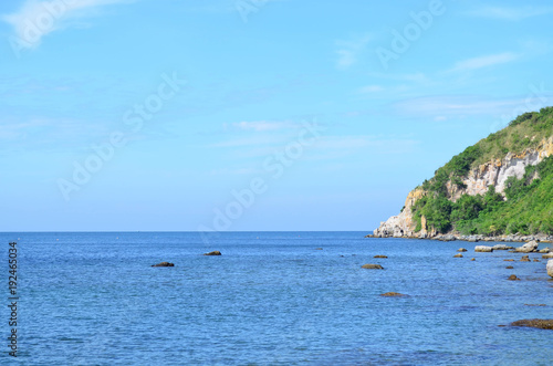 Beautiful calm sea with rock and mountain on blue sky day