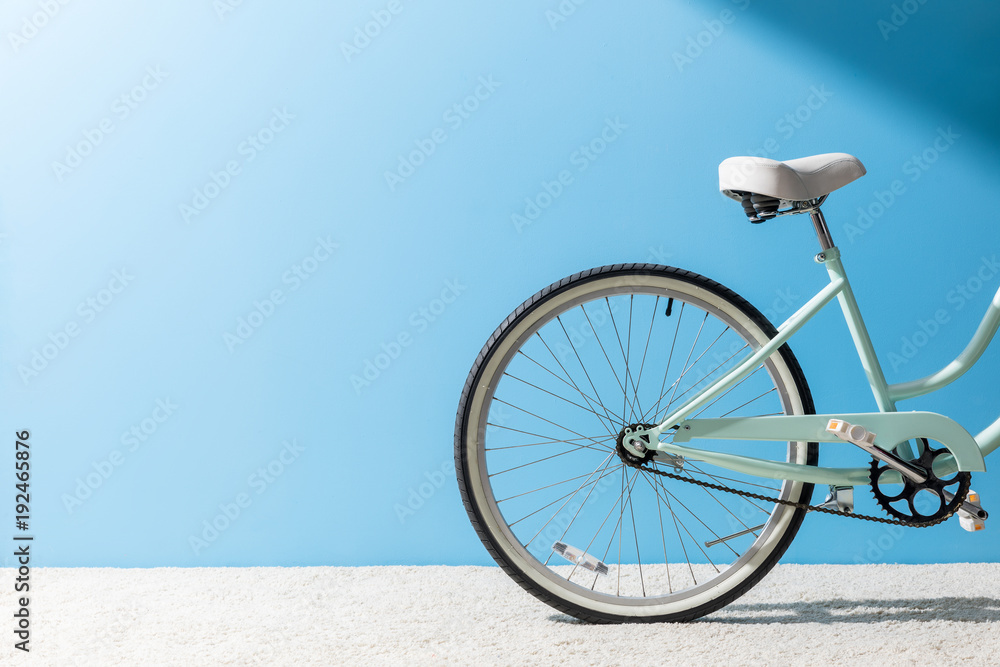 back wheel of bicycle standing on carpet in front of blue wall - obrazy, fototapety, plakaty 