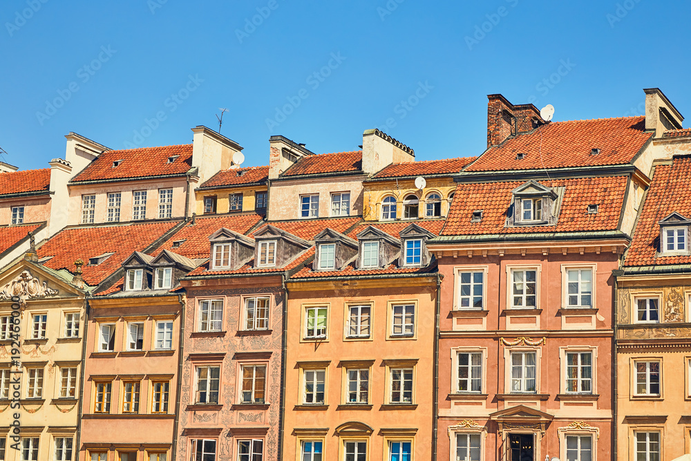 Facades of houses with windows and roofs against the blue sky on a clear sunny day in the old town in Warsaw, Poland Facades of houses with windows and roofs against the blue sky on a clear sunny day in the old town in Warsaw, Poland